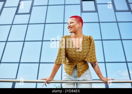 Une femme chauve vibrante sourit avec éclat tout en s'appuyant sur une balustrade de balcon dans un décor saisissant. Banque D'Images