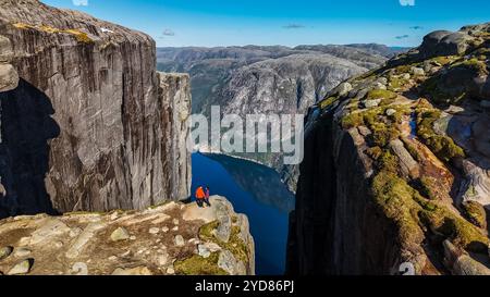 Deux individus se tiennent au bord du Kjeragbolten, falaise de Norvège, donnant sur une vue imprenable sur le fjord Banque D'Images