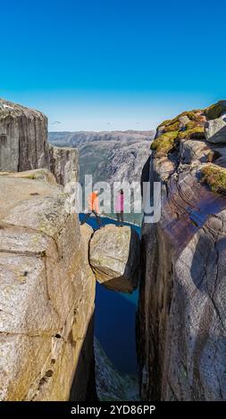 Deux individus se tiennent au bord de Kjeragbolten, une falaise en Norvège, surplombant une vue imprenable sur le paysage environnant. Banque D'Images