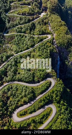 Une vue aérienne d'une route sinueuse serpentant à travers un paysage norvégien verdoyant, avec une cascade en arrière-plan Banque D'Images