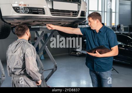 Un mécanicien s'adresse à un directeur dans le cadre d'un service de véhicule en voiture. Bossage montrant ce qu'il faut corriger Banque D'Images