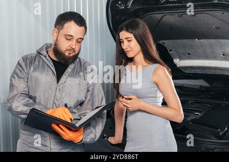 Auto Mechanic explique la facture de réparation du véhicule au client féminin et les documents de signature Banque D'Images