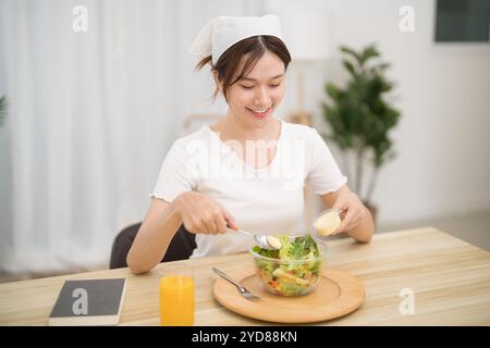 Heureuse belle femme asiatique mangeant des aliments sains avec de la salade végétalienne dans la cuisine à la maison Banque D'Images