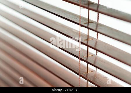 Gros plan de stores en bois à lattes horizontales, mettant en valeur la texture et les détails du bois. La lumière filtre à travers les espaces, créant un diff doux Banque D'Images