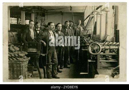 Original, clair début des années 1900 carte postale des ouvriers d'usine masculins, avec le contremaître ou le patron à côté d'eux. Des hommes édouardiens. Ce sont des hommes de la classe ouvrière, dans un atelier d'assemblage de machines / monteurs debout à côté des machines et des équipements industriels qu'ils ont fabriqués. Sur le devant de la photo se trouvent de nombreuses roues en métal dans le panier. Ceux-ci ressemblent à des roues en acier pour les bandes transporteuses appelées rouleaux de renvoi, également appelés rouleaux de convoyeur. Utilisé dans des industries telles que l'extraction du charbon. Il y en a une pile en arrière-plan aussi. Peut-être Yorkshire ou Lancashire, où l'exploitation minière était basée. Angleterre, Royaume-Uni circa 1910 Banque D'Images