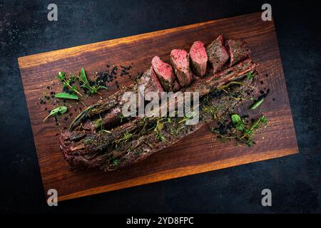 Selle de gibier rôtie traditionnellement avec des morceaux de filet et des herbes servait de vue de dessus sur une planche à découper design en bois Banque D'Images