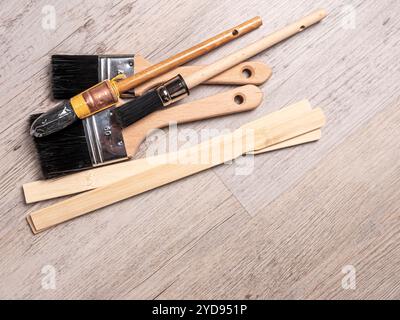 Nettoyer les brosses et les bâtons pour mélanger la peinture sur un plancher en bois. Banque D'Images