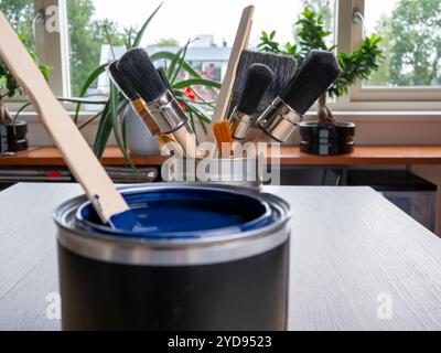 Nettoyez les pinceaux et les bâtons de mélange de peinture dans une boîte de fer. Une boîte de peinture bleue dans un premier plan flou. Banque D'Images