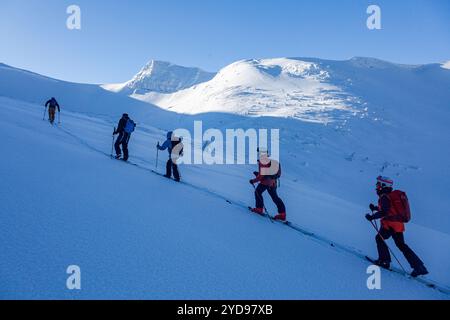 Les skieurs de l'arrière-pays grimpent en une seule ligne et remontent la pente enneigée des montagnes, avec un soleil éclatant sur la neige. Banque D'Images