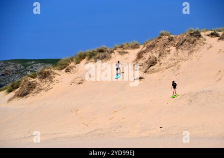 Deux jeunes gens Sand Surfing sur les dunes sur Holywell Beach près de Newquay sur le sentier côtier du Sud-Ouest, Cornouailles du Nord, Angleterre, Royaume-Uni Banque D'Images