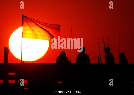 Île de Palms, États-Unis. 25 octobre 2024. Pêcheurs silhouettés par le lever du soleil, regardez le soleil orange géant se lever sur l'océan Atlantique depuis l'embarcadère de l'île de Palms sur Front Beach, le 25 octobre 2024 à l'île de Palms, Caroline du Sud. Un temps ensoleillé et chaud est prévu pour le pays bas pour les prochaines semaines. Crédit : Richard Ellis/Richard Ellis/Alamy Live News Banque D'Images