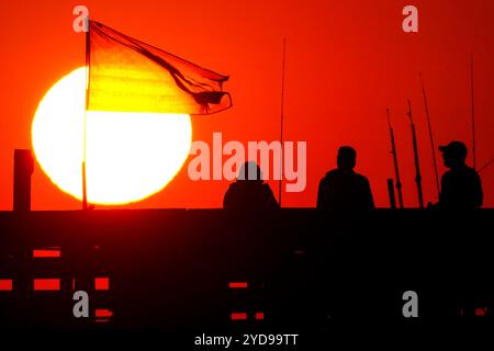 Île de Palms, États-Unis. 25 octobre 2024. Pêcheurs silhouettés par le lever du soleil, regardez le soleil orange géant se lever sur l'océan Atlantique depuis l'embarcadère de l'île de Palms sur Front Beach, le 25 octobre 2024 à l'île de Palms, Caroline du Sud. Un temps ensoleillé et chaud est prévu pour le pays bas pour les prochaines semaines. Crédit : Richard Ellis/Richard Ellis/Alamy Live News Banque D'Images