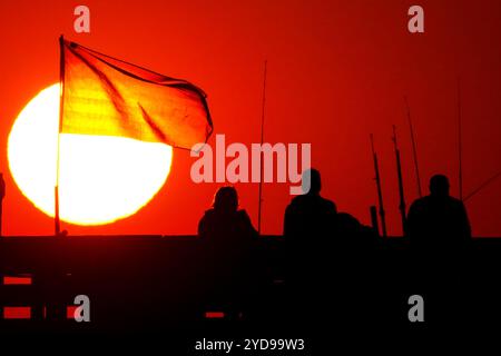 Île de Palms, États-Unis. 25 octobre 2024. Pêcheurs silhouettés par le lever du soleil, regardez le soleil orange géant se lever sur l'océan Atlantique depuis l'embarcadère de l'île de Palms sur Front Beach, le 25 octobre 2024 à l'île de Palms, Caroline du Sud. Un temps ensoleillé et chaud est prévu pour le pays bas pour les prochaines semaines. Crédit : Richard Ellis/Richard Ellis/Alamy Live News Banque D'Images