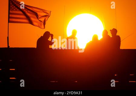 Île de Palms, États-Unis. 25 octobre 2024. Pêcheurs silhouettés par le lever du soleil, regardez le soleil orange géant se lever sur l'océan Atlantique depuis l'embarcadère de l'île de Palms sur Front Beach, le 25 octobre 2024 à l'île de Palms, Caroline du Sud. Un temps ensoleillé et chaud est prévu pour le pays bas pour les prochaines semaines. Crédit : Richard Ellis/Richard Ellis/Alamy Live News Banque D'Images