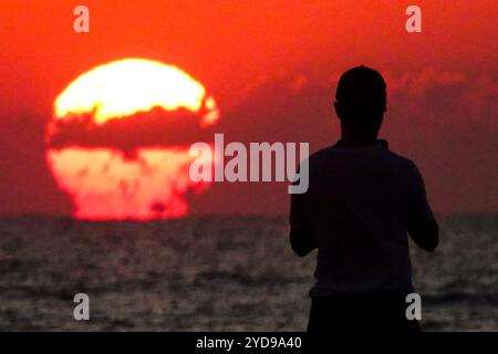 Île de Palms, États-Unis. 25 octobre 2024. Un touriste silhouetté par le lever du soleil, prend une photo alors que le soleil orange géant se lève au-dessus de l'horizon atlantique sur Front Beach, le 25 octobre 2024 à Isle of Palms, Caroline du Sud. Un temps ensoleillé et chaud est prévu pour le pays bas pour les prochaines semaines. Crédit : Richard Ellis/Richard Ellis/Alamy Live News Banque D'Images