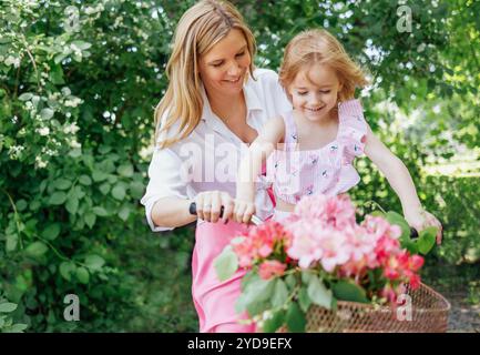 Une jeune mère attrayante fait un vélo avec sa petite fille mignonne. Une charmante femme blonde et une fille joyeuse qui rit s'amusent. Une flowerin Banque D'Images