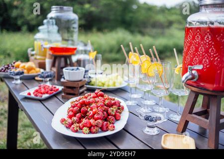 Une table en bois avec des baies et des fruits sucrés, des pots de jus fraîchement pressé et des verres vides. Un buffet d'été en plein air. Banque D'Images