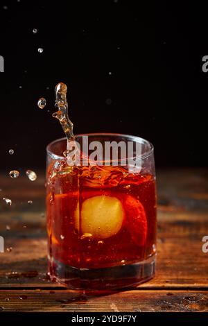 Cocktail alcoolisé Negroni ou cocktail non alcoolisé avec éclaboussure dans le verre, boire avec de la glace et de l'écorce d'orange comme décoration sur table en bois Banque D'Images