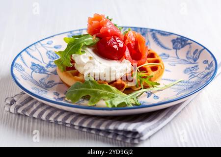 Gaufres belges pour le petit déjeuner sur une assiette blanche. Gaufres au saumon, fromage à la crème, roquette et tomates cerises. Banque D'Images