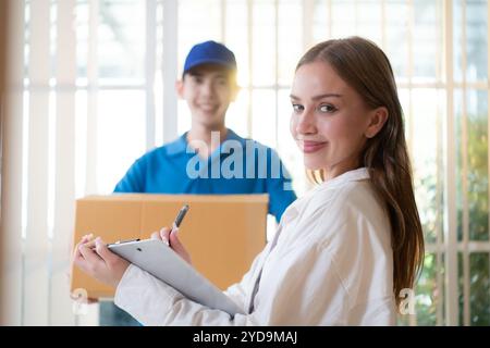 La fille signe le document de presse-papiers avant de ramasser les articles de l'homme, qui tient les produits dans une boîte en carton i. Banque D'Images