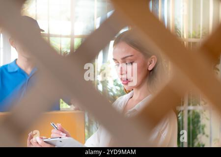 La fille signe le document de presse-papiers avant de ramasser les articles de l'homme, qui tient les produits dans une boîte en carton i. Banque D'Images