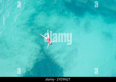 Vue aérienne de dessus d'une femme portant un maillot de bain rouge couché sur la surface de l'eau turquoise transparente sur la plage des caraïbes. Voyage et vacati Banque D'Images