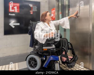 Utilisateur de fauteuil roulant électrique appuyant sur le bouton de l'ascenseur dans le métro Banque D'Images