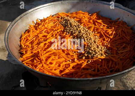 Cuisson du pilaf dans un grand chaudron, avec des carottes et des pois chiches jetés dans la casserole avec de l'huile pour la friture. Banque D'Images