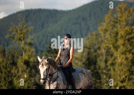 cavalier féminin guide son cheval en toute confiance à travers un terrain accidenté de montagne, jetant un coup d'œil à la caméra avec une expression calme, capturant l'aventuro Banque D'Images