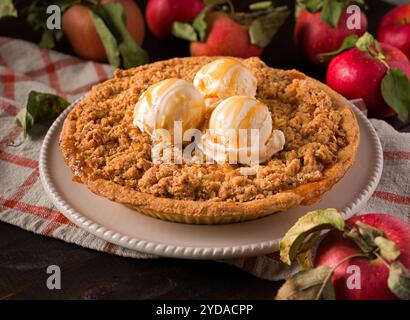 Gros plan d'une tarte à la chapelure de pommes dans une assiette blanche avec des pommes fraîchement cueillies, surmontées de trois boules de glace à la vanille Banque D'Images