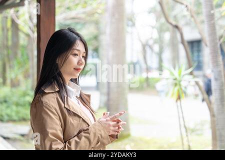 Une taïwanaise aux cheveux longs dans la vingtaine portant un trench beige passe son après-midi d'hiver sous les avant-toiTS dans le district de Xinyi, Taipei, Taiwan, on Banque D'Images