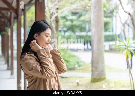 Une taïwanaise aux cheveux longs dans la vingtaine portant un trench beige passe son après-midi d'hiver sous les avant-toiTS dans le district de Xinyi, Taipei, Taiwan, on Banque D'Images