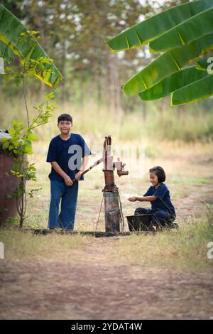 L'enfance en Thaïlande rurale. Un petit enfant aide sa famille en pompant de l'eau naturelle dans un seau Banque D'Images
