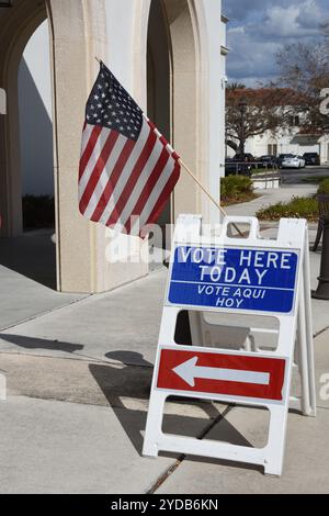 Venise, Floride, États-Unis – 24 octobre 2024 : drapeau américain et tableau sandwich avec le message « votez ici aujourd'hui » avec une flèche pointant vers le bureau de vote. Banque D'Images