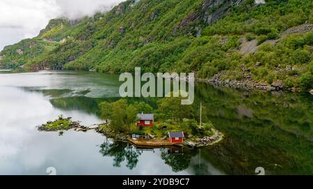 Deux cabines rouges se trouvent sur une petite île luxuriante entourée d'eau calme et verte. Lovrafjorden, Norvège Banque D'Images