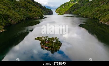 Une petite île avec deux maisons rouges est nichée dans un fjord calme entouré de collines boisées verdoyantes. Lovrafjorden, Norvège Banque D'Images