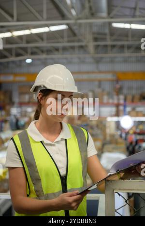 Travailleuse d'entrepôt comptant des articles dans un entrepôt industriel sur le plancher de mezzanine de l'usine. ce qui est un stockage pour les petits Banque D'Images