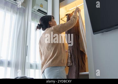 Fille asiatique préparant des vacances en choisissant des vêtements avec garde-robe dans la chambre avant le voyage de vacances Banque D'Images