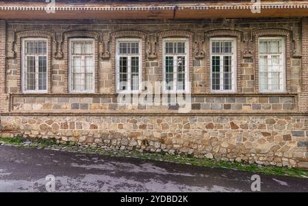 Ce cadre dispose d'un bâtiment historique en pierre présentant plusieurs fenêtres ornées. Il reflète des éléments architecturaux classiques, enveloppés par un paysage de village tranquille Banque D'Images