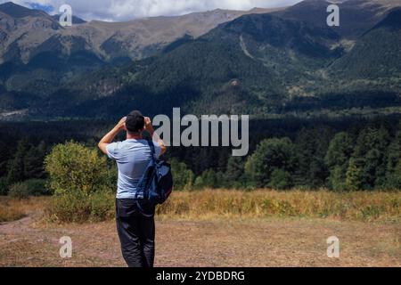 Jeune homme dans des vêtements décontractés avec sac à dos prend des photos de paysage sur son téléphone. Vue arrière. Touriste prend des photos du mont Banque D'Images