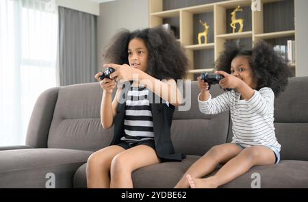 Deux frères d'une famille afro-américaine asiatique. Détendez-vous et jouez à des jeux en ligne dans le salon de la maison. Banque D'Images