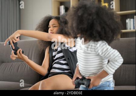 Deux frères d'une famille afro-américaine asiatique. Détendez-vous et jouez à des jeux en ligne dans le salon de la maison. Banque D'Images