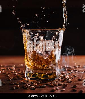 Splash de whisky d'un cube de glace dans le verre Banque D'Images