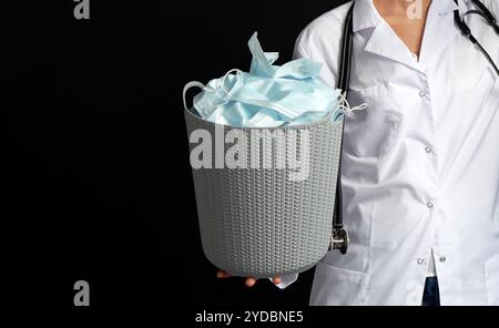 Le médecin tient un seau rempli de masques faciaux usagés, les jetant comme symbole de fin d'épidémie Banque D'Images