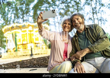 Couple senior prenant selfie assis sur le banc dans une foire de la ville de nuit Banque D'Images