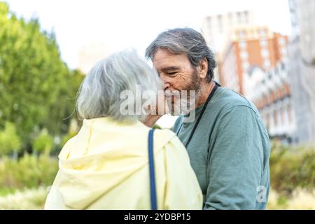 Photo en gros plan d'un couple d'aînés modernes caucasiens s'embrassant debout dans un parc urbain Banque D'Images