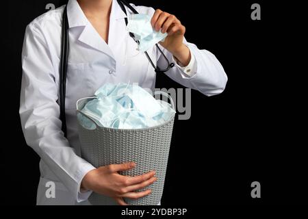 Le médecin tient un seau rempli de masques faciaux usagés, les jetant comme symbole de fin d'épidémie Banque D'Images