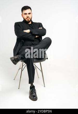 Jeune homme handicapé avec prothèse de jambe assise sur une chaise en studio sur fond blanc, concept de membre artificiel Banque D'Images