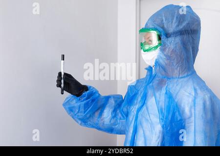 Technologue en soins médicaux tenant un écouvillon COVID-19, portant un vêtement de protection EPI, un masque, des gants. Tube a essai pour PRELEVER OP NP Pat Banque D'Images