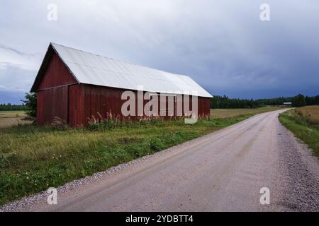 Grange rouge à côté d'une route de gravier dans un paysage rural en Finlande Banque D'Images